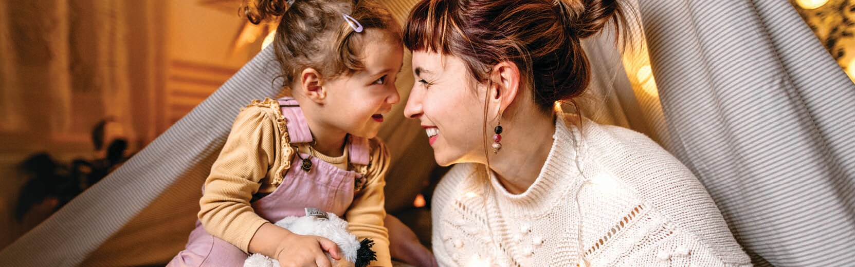 Mother and daughter smiling at each other while in a blanket tent.